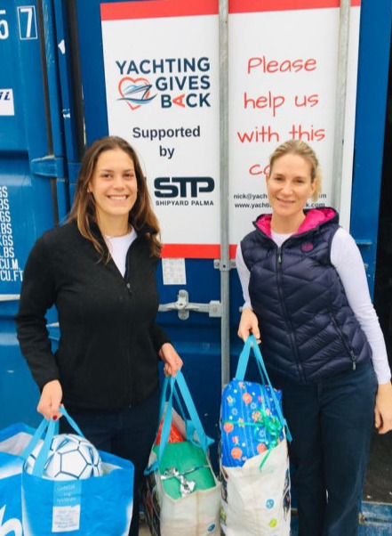 Two women holding bags of donations next to the YGB container