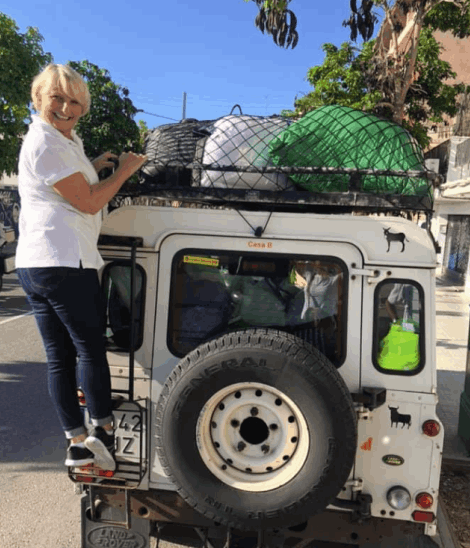 A woman packing bags on the roof rack of a Land Rover