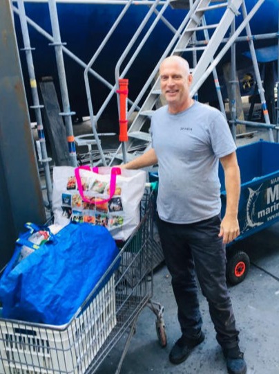 A man with a shopping trolley full of donations next to a yacht in the shipyard