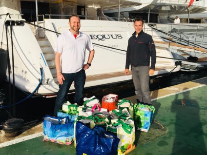Two men with bags of donations behind a yacht