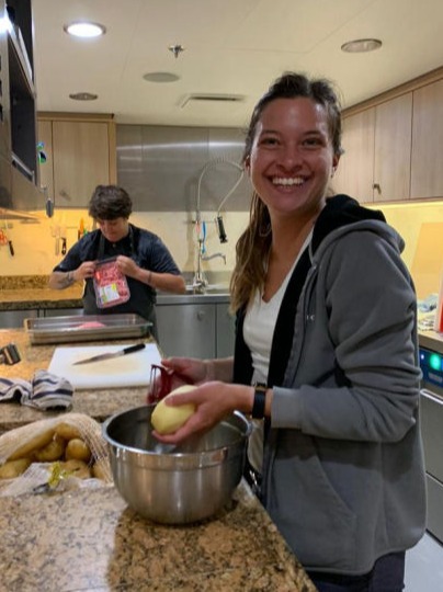 A smiling woman peeling potatoes in the galley