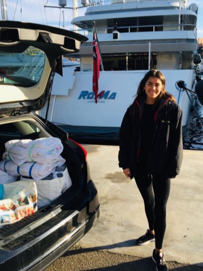 A woman with a car boot full of donations behind a yacht
