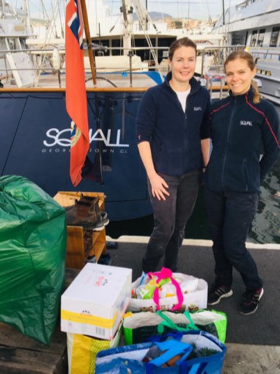 Two women with bags of donations behind a yacht 