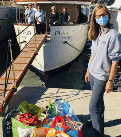 A volunteer from YGB stands in front of a yacht and next to bags of items donated by the yacht